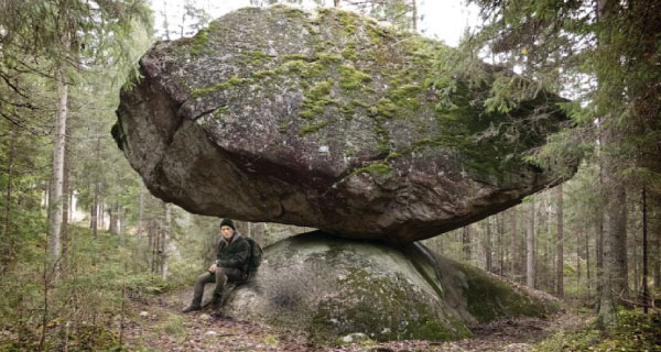 Man sitting under a giant boulder